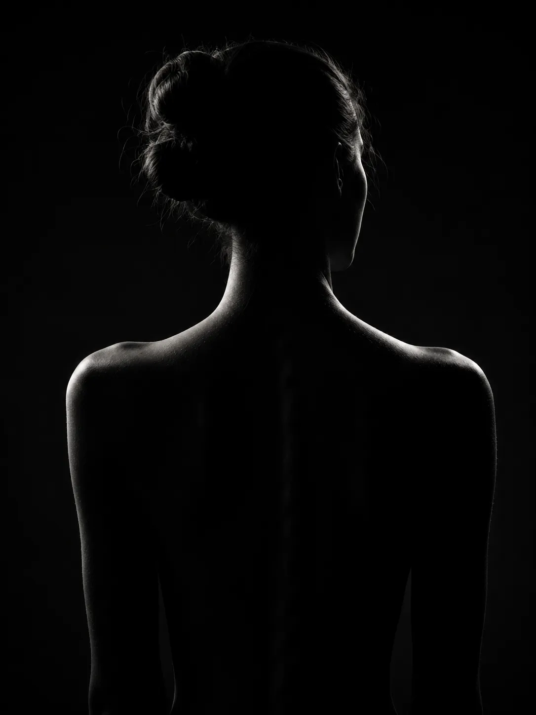 Rear-view silhouette of a woman with her hair in a bun, outlined by soft rim lighting