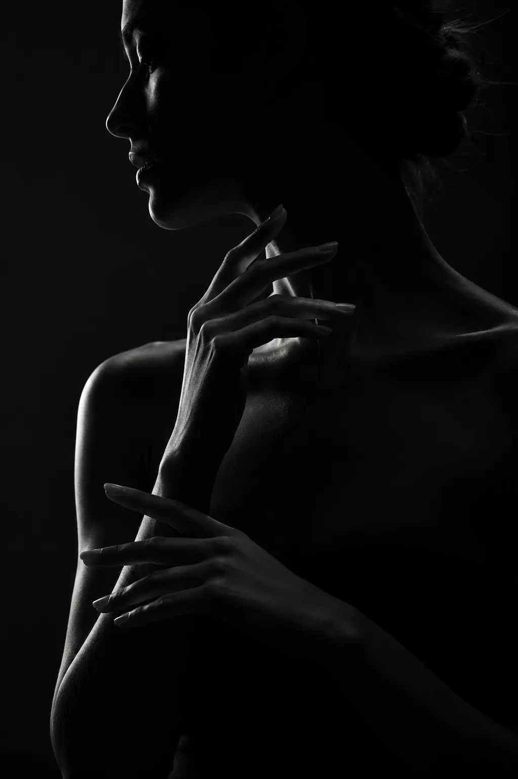 Dark side-profile portrait of a woman with one hand raised near her neck