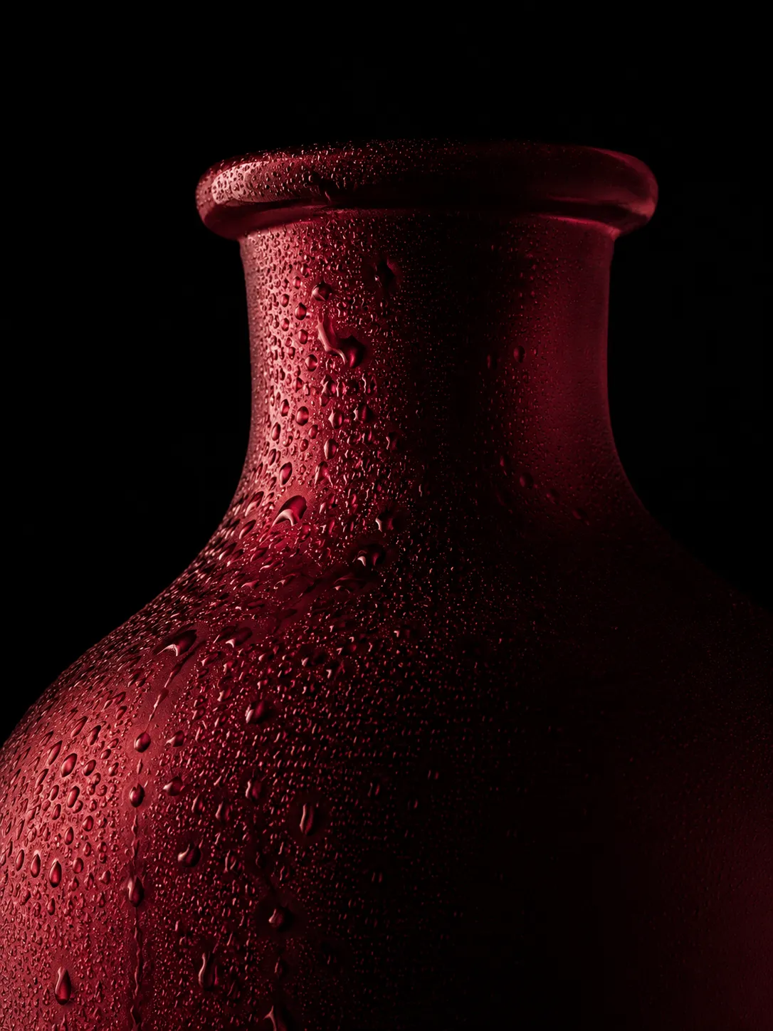 Crimson glass vase covered with water droplets against a black background.