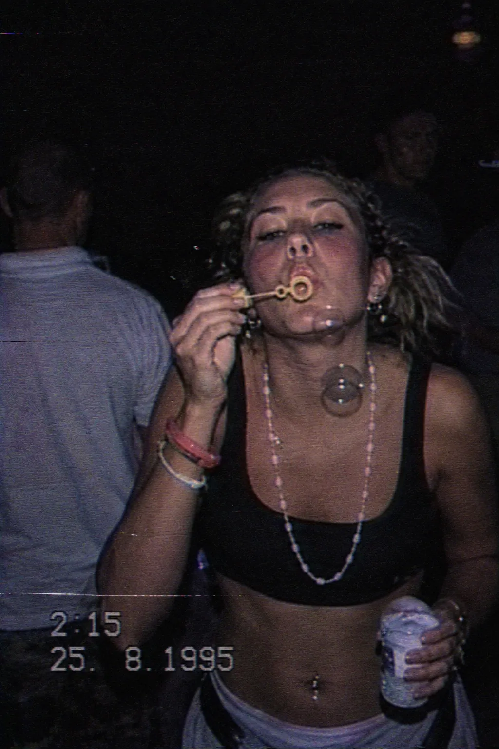 Young woman at a night rave blowing bubbles, in a black crop top and beaded necklaces