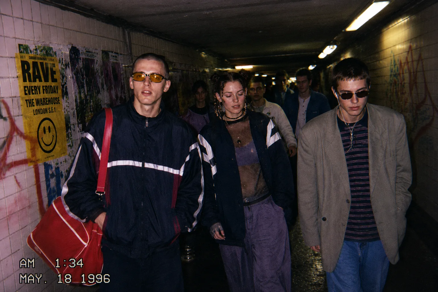 Three young ravers in 90s sportswear walking through a tiled London underpass 