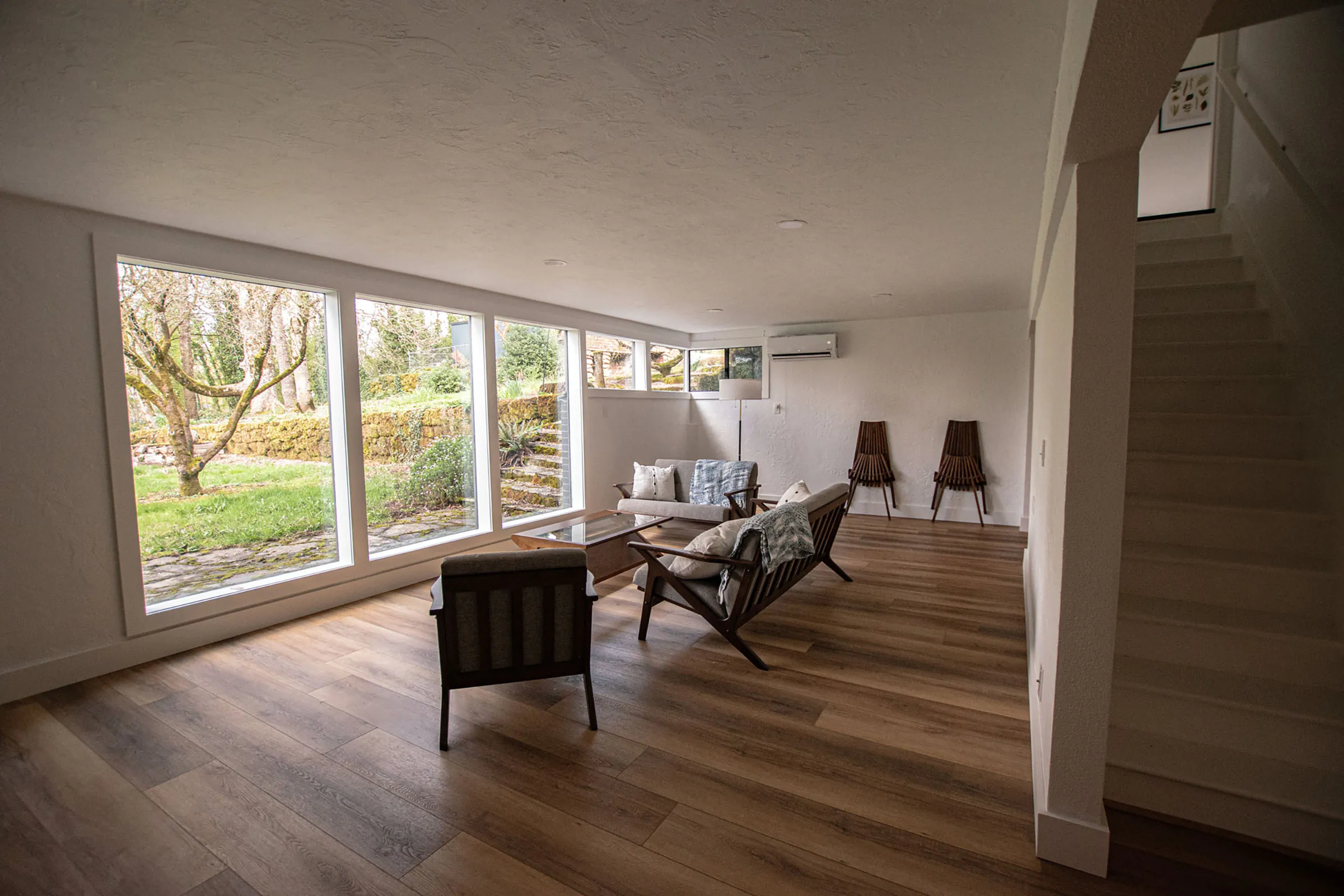 Mt. Scott daylight basement living area with large windows, staircase, and wood-look floors