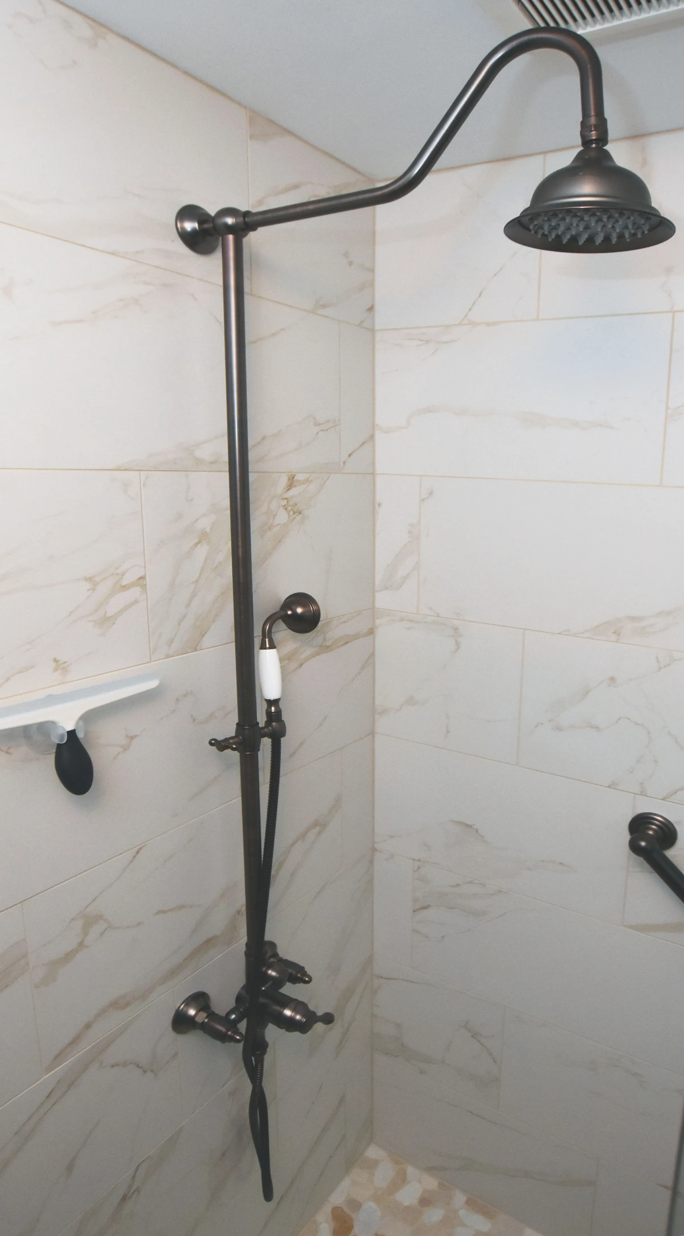 Gladstone shower with marble-look tile, bronze rain showerhead, handheld sprayer, and grab bar