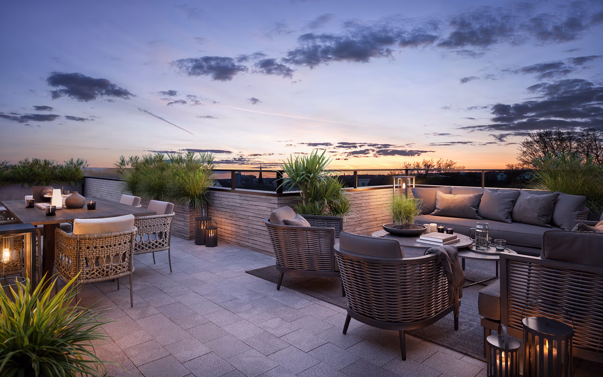 Cozy rooftop terrace with seating, dining table, plants, and lanterns under a colorful sunset sky.