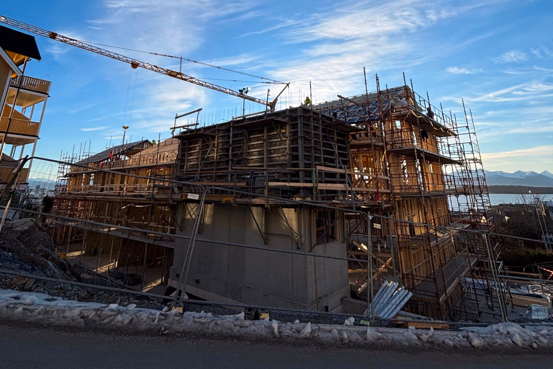 Large building under construction with scaffolding and a crane against a blue sky.