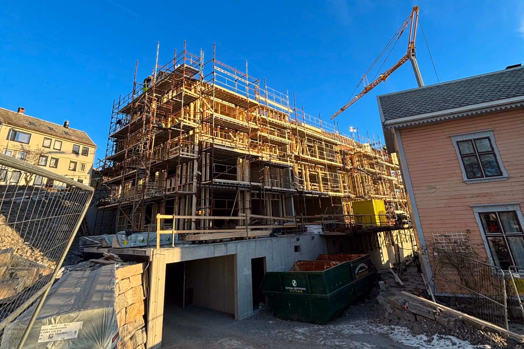 Multi-story building under construction with scaffolding and crane against a clear blue sky.