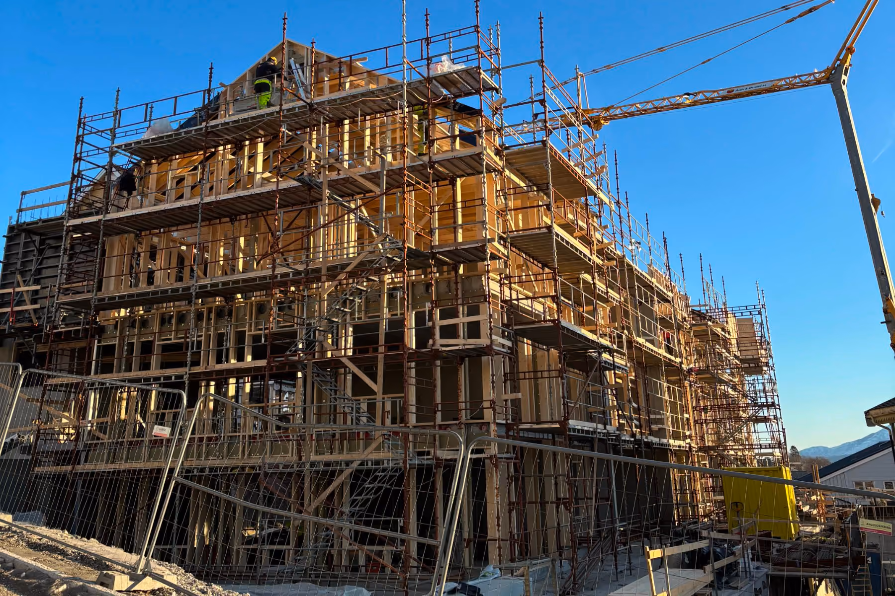 Wooden building under construction with scaffolding and workers against a clear blue sky.