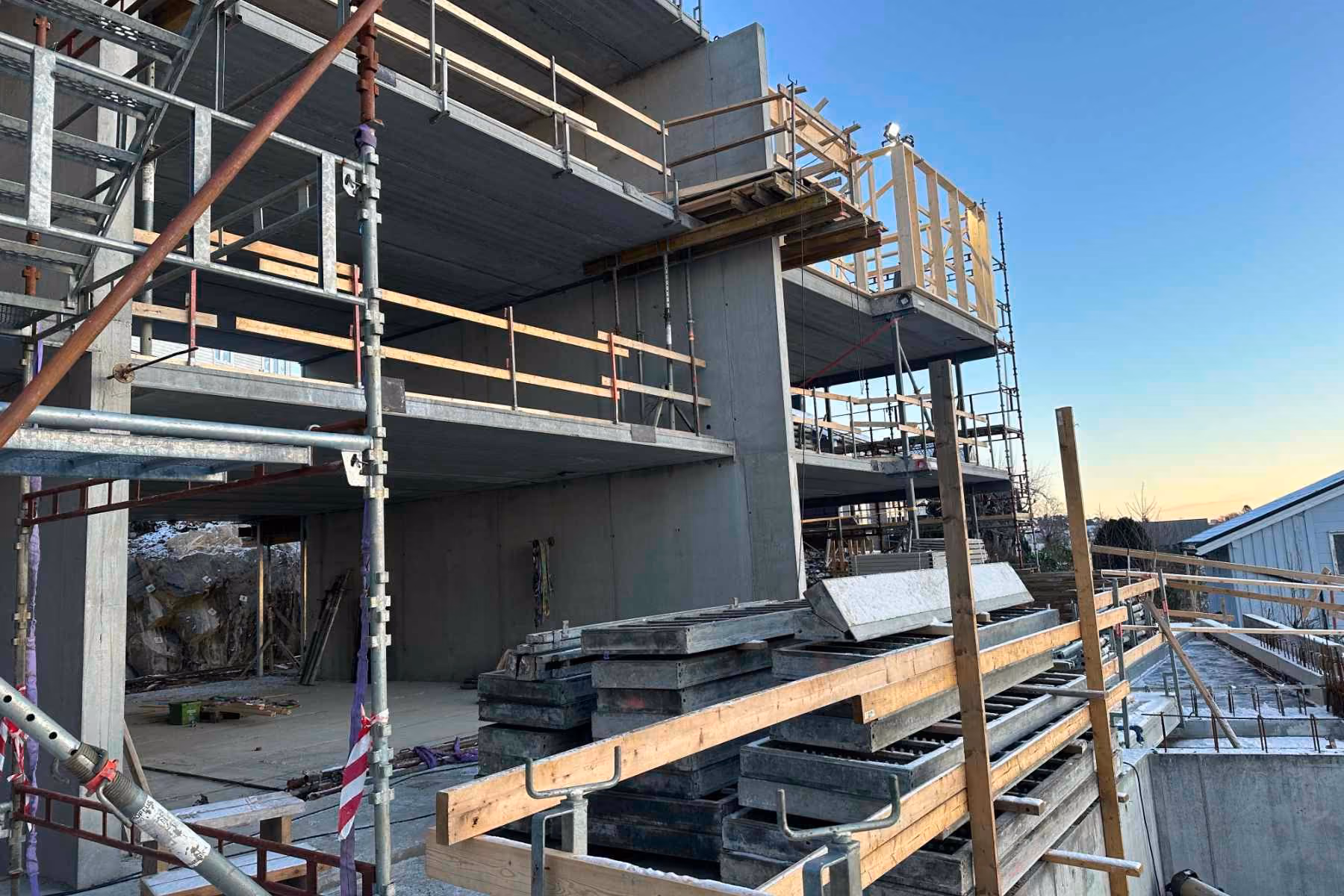 Partially constructed concrete building with scaffolding, stacks of construction materials, and wood railings.