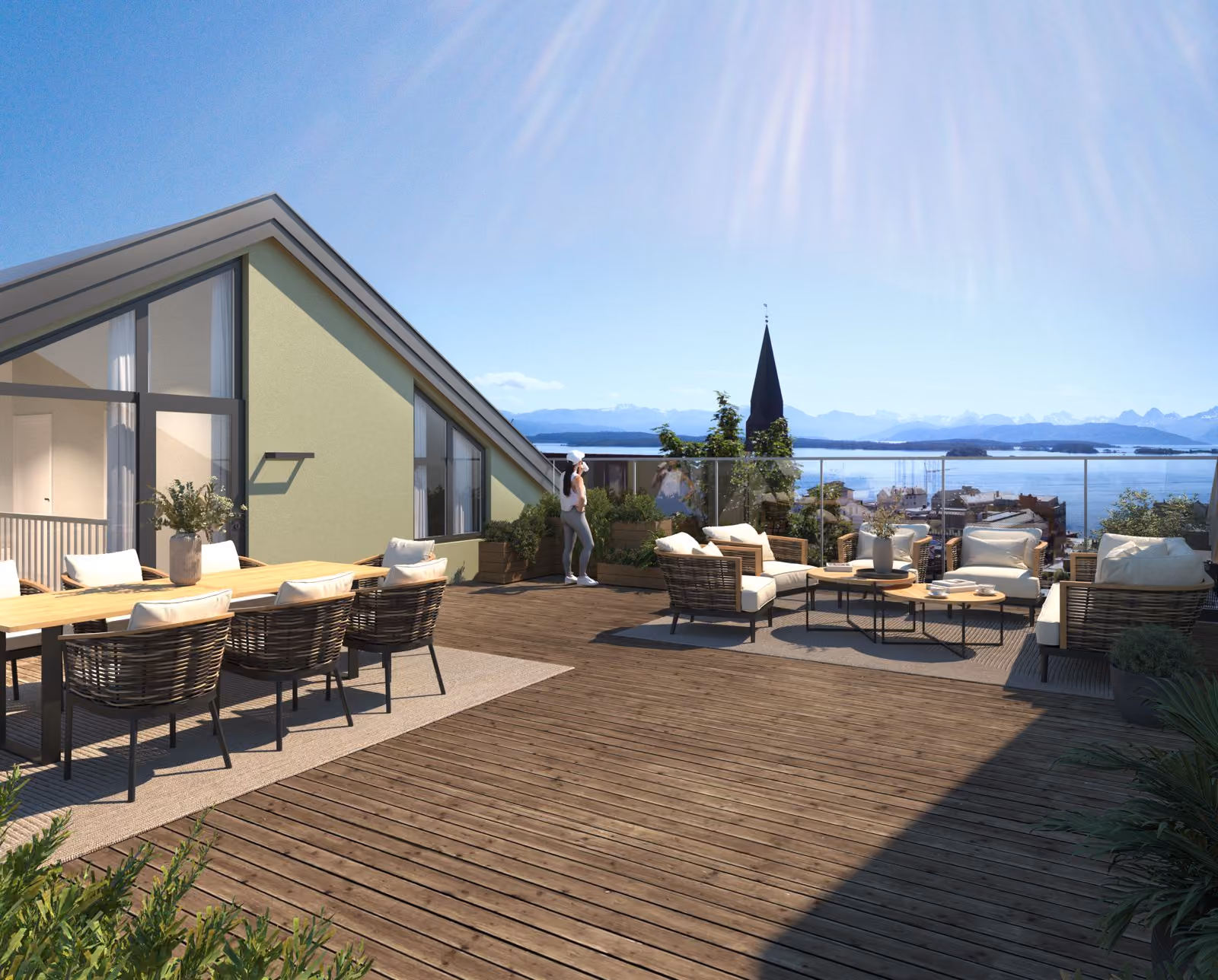 Spacious balcony with seating and dining areas overlooking water and mountain landscape on a sunny day.