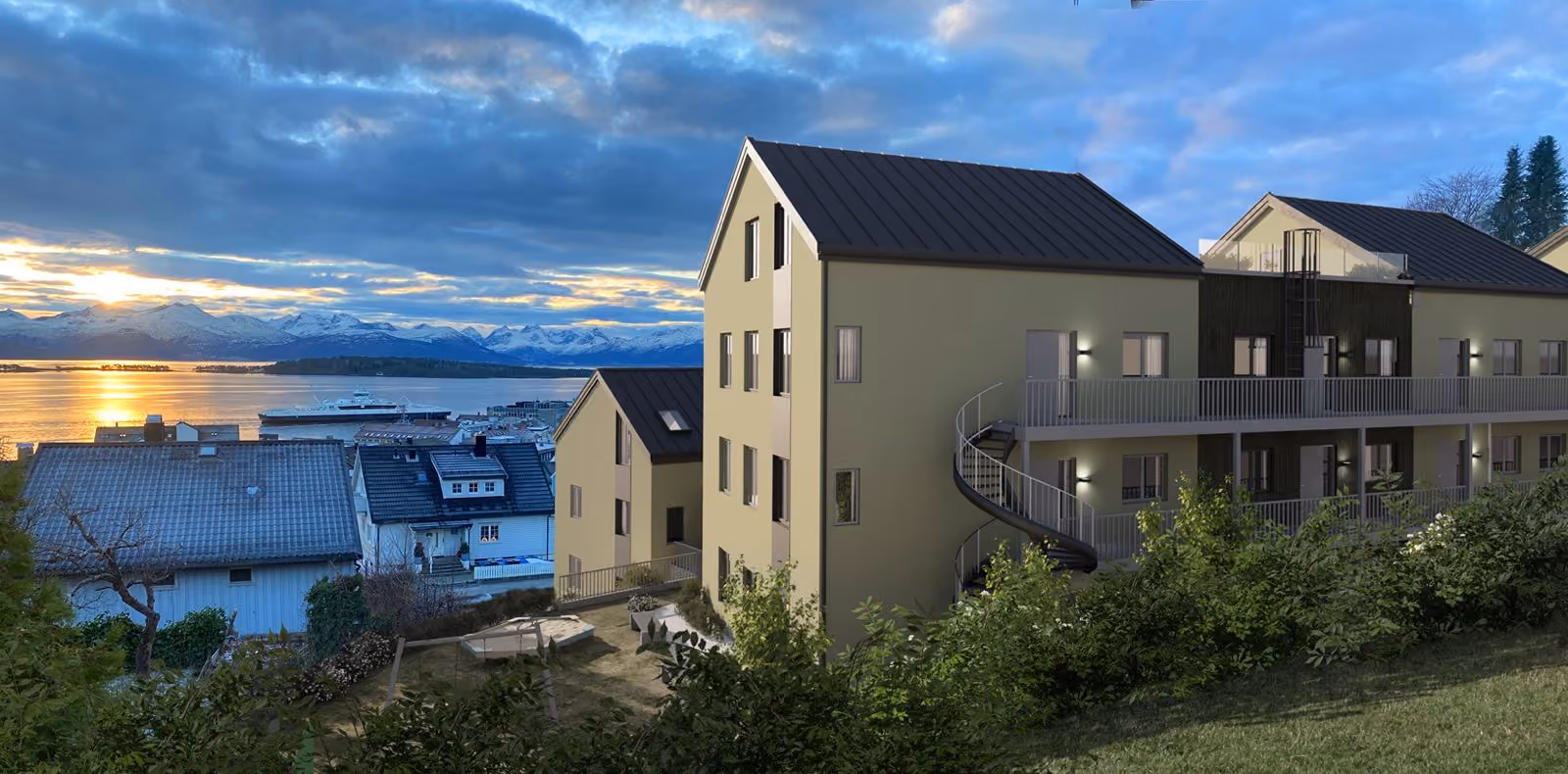 Modern residential buildings on a hillside overlooking a body of water with a sunset and mountains.