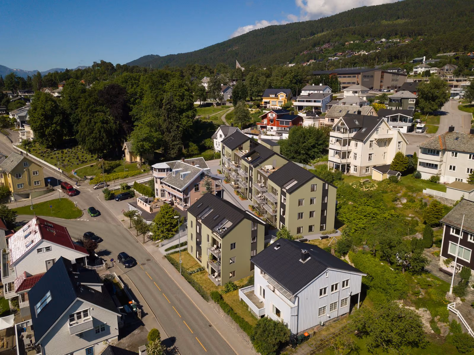 Aerial view of a residential neighborhood with modern houses, trees, and roads on a sunny day.