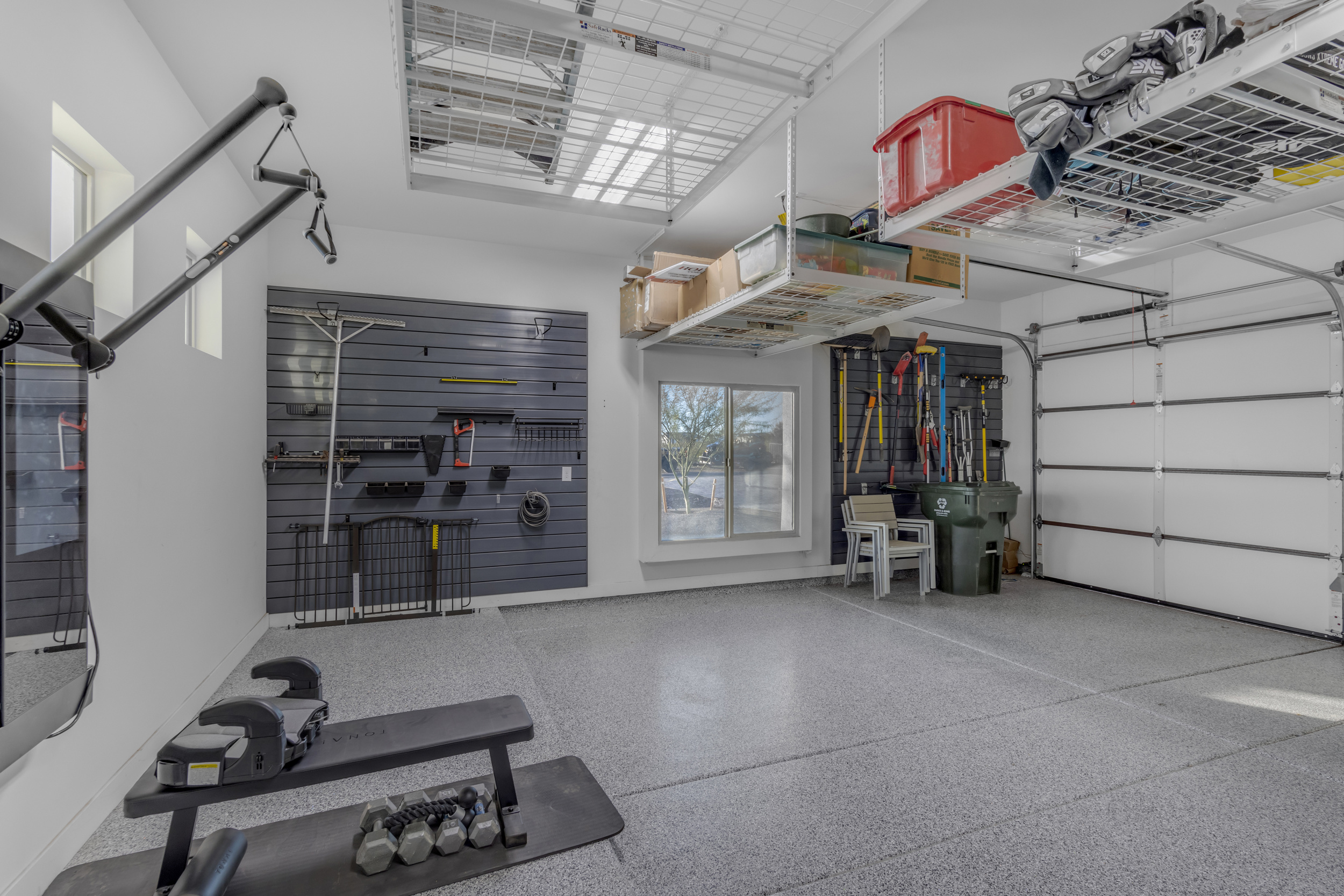 Clean, organized garage with exercise equipment, wall-mounted tools, and overhead storage racks.