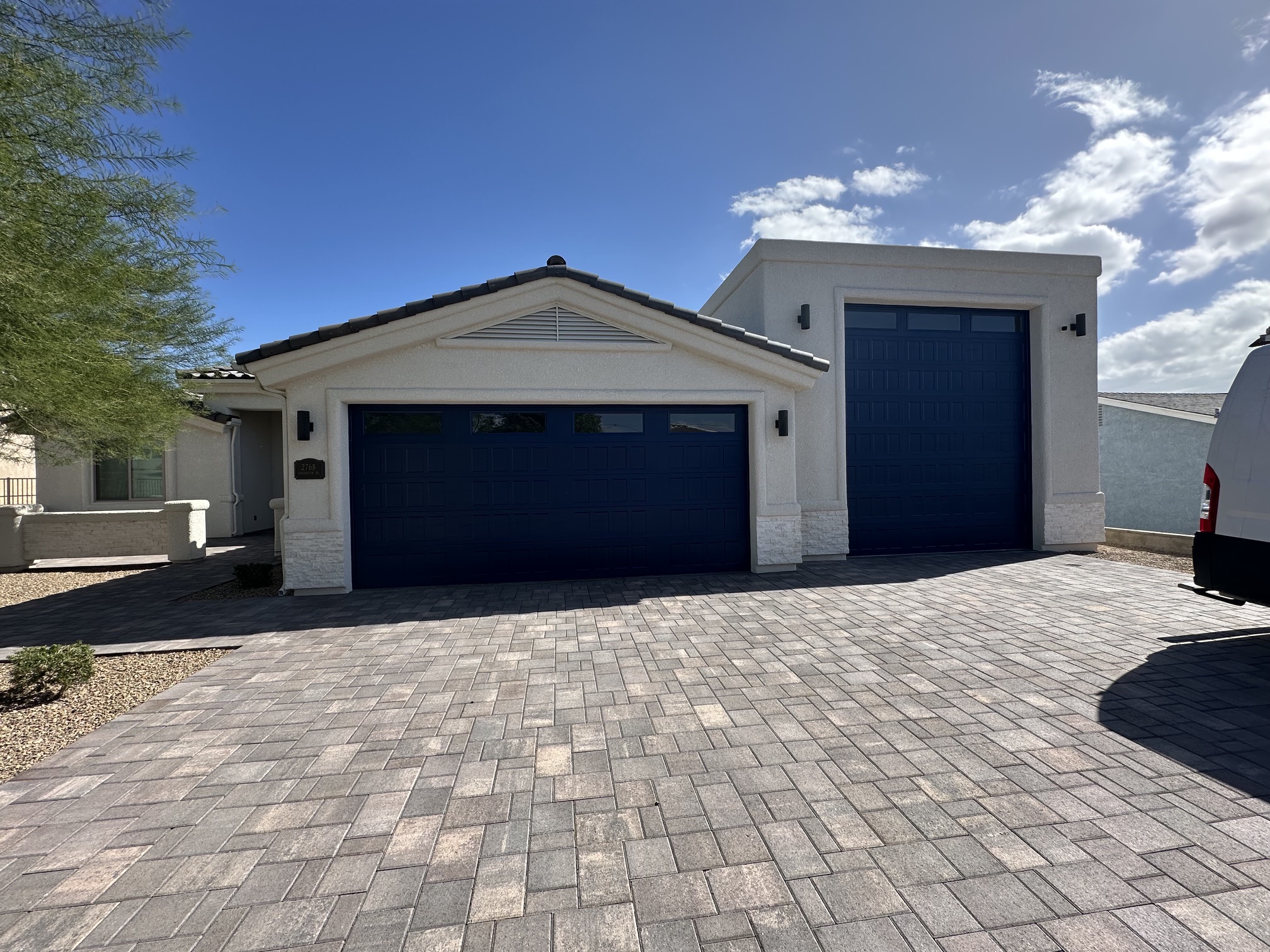 Modern house exterior with two dark blue garage doors and paved driveway under a clear sky.