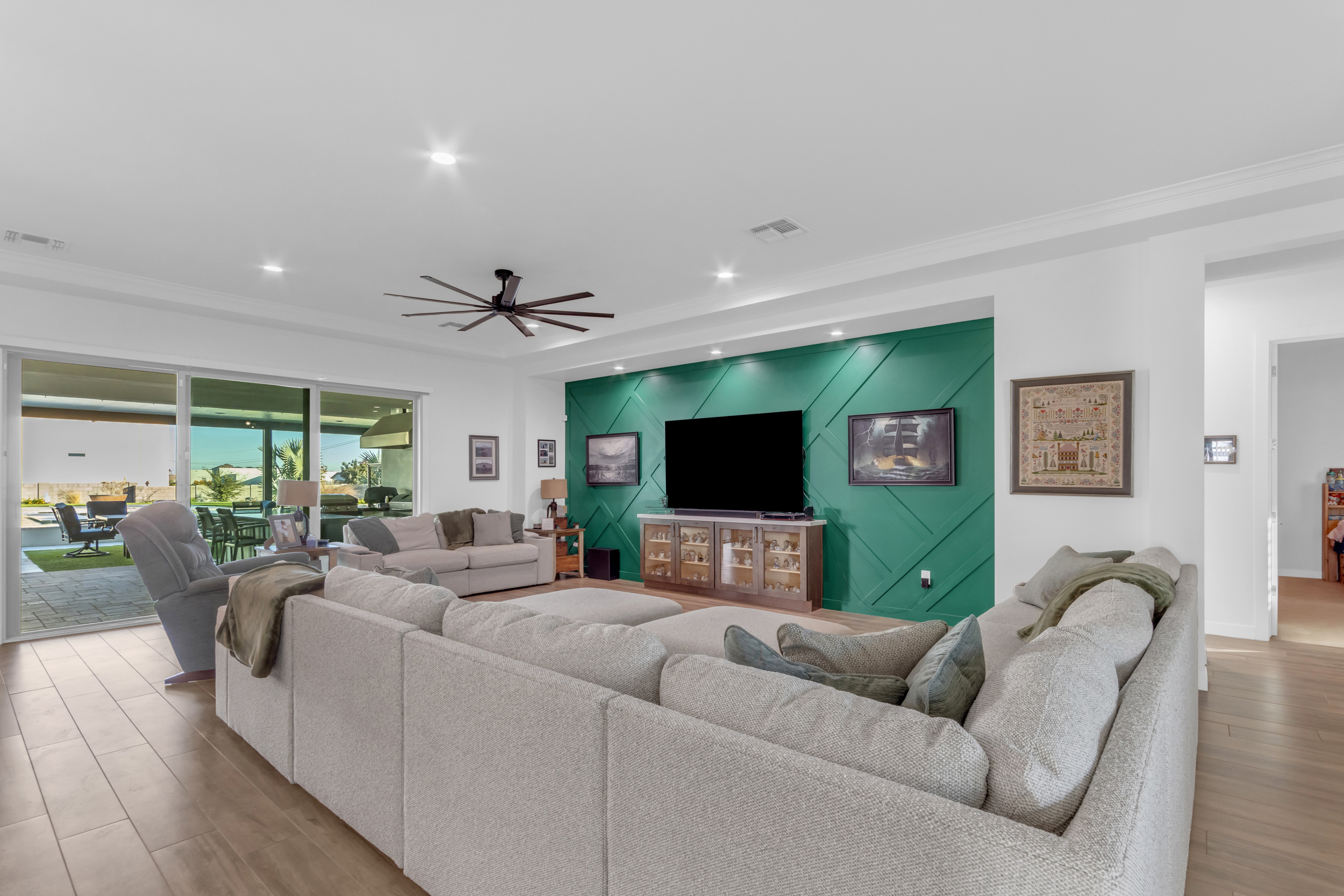 Modern living room with beige sectional sofa, green accent wall, large TV, and sliding glass doors to patio.