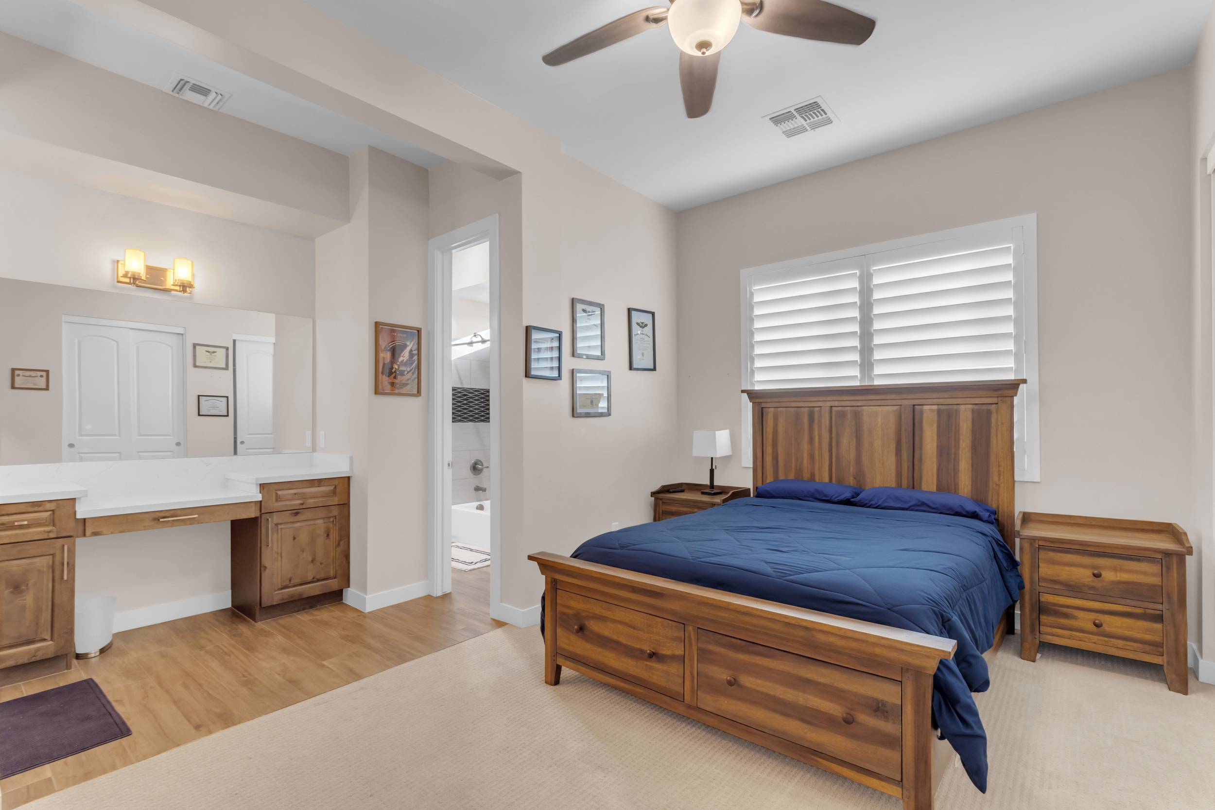 Bedroom with wooden bed, blue bedding, two nightstands, ceiling fan, and a vanity area with mirror.