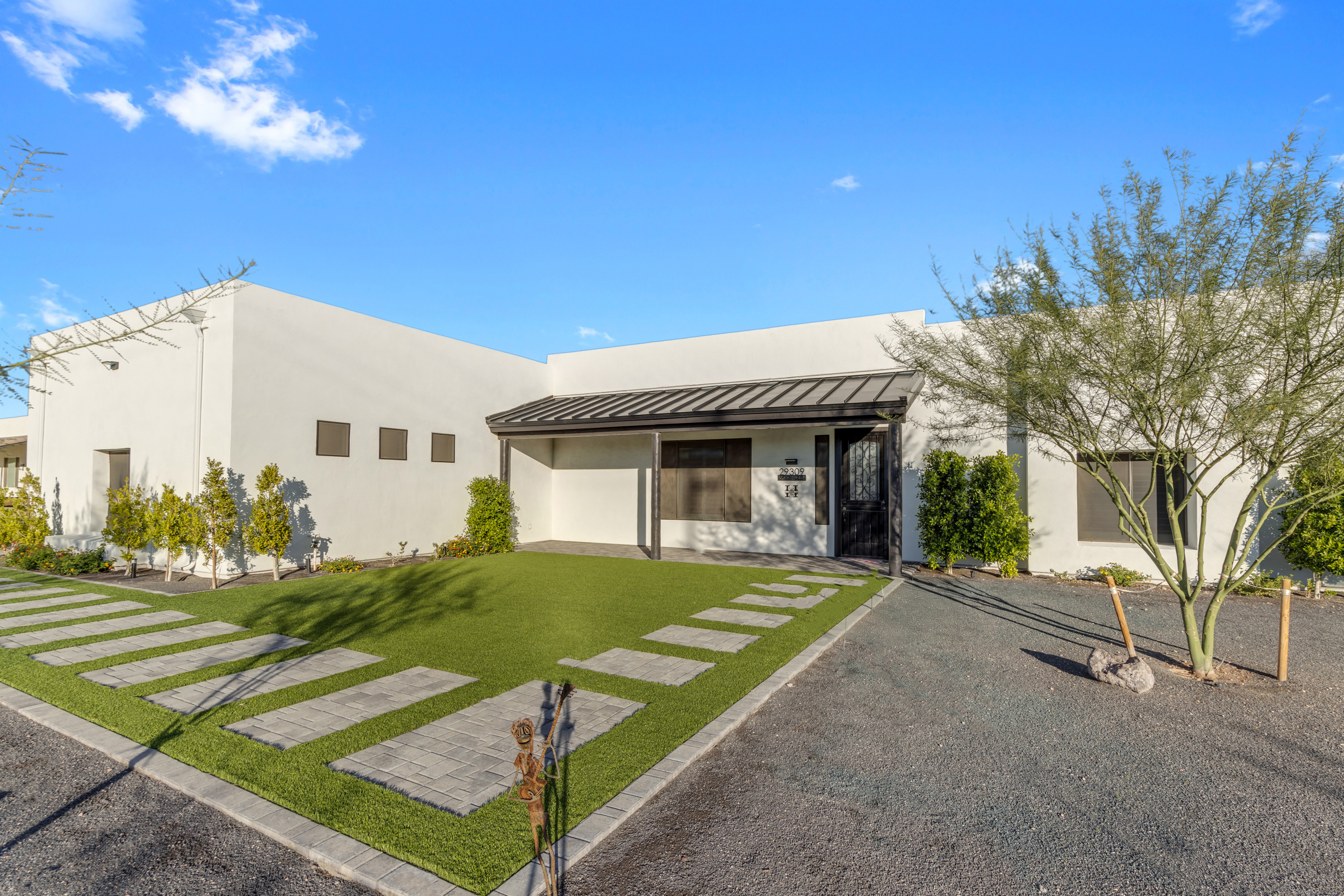 Modern white house with a metal porch roof, green lawn, stone walkway, and sparse desert landscaping.