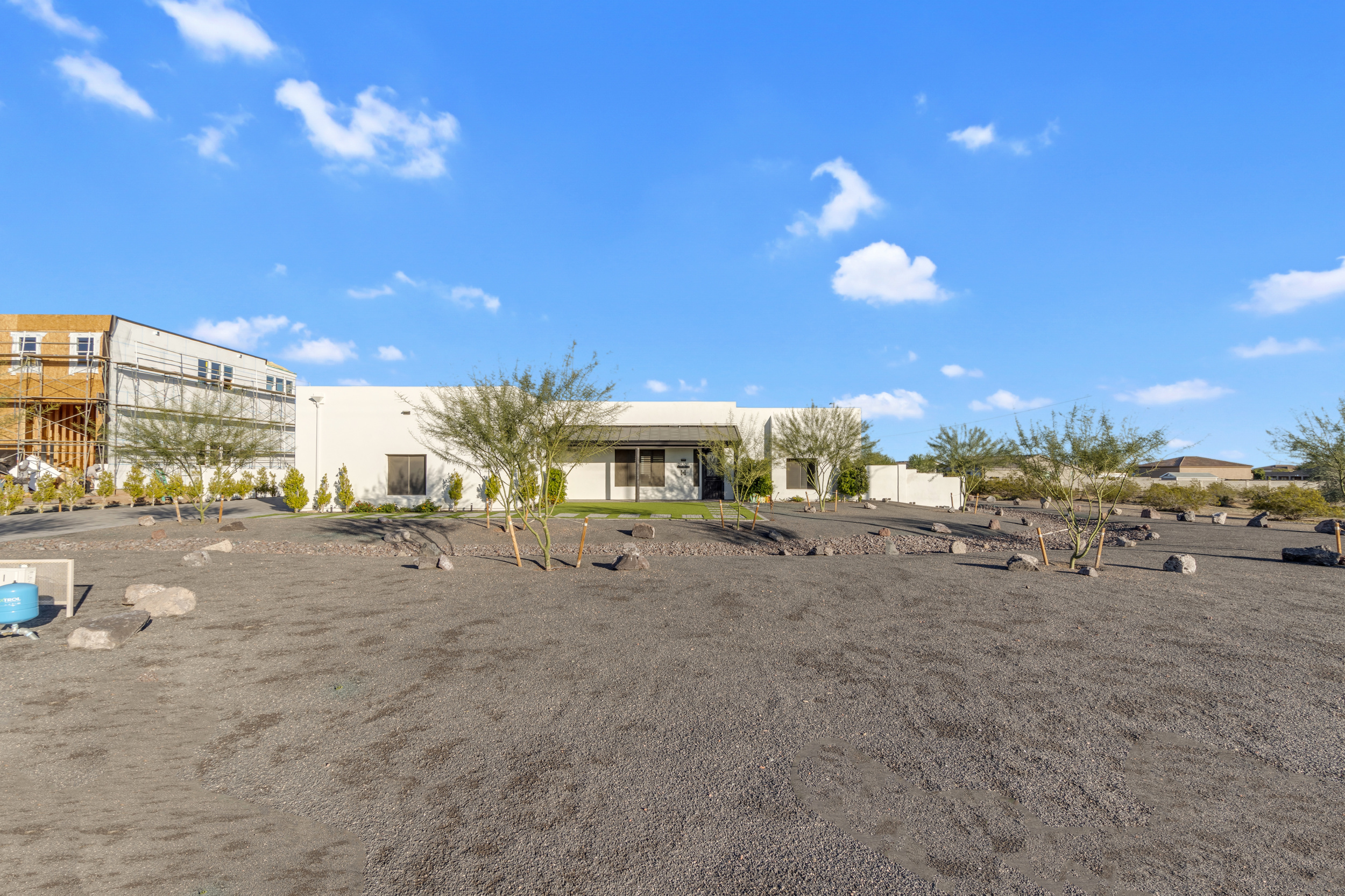 Modern white house with sparse desert landscaping under a blue sky with scattered clouds.