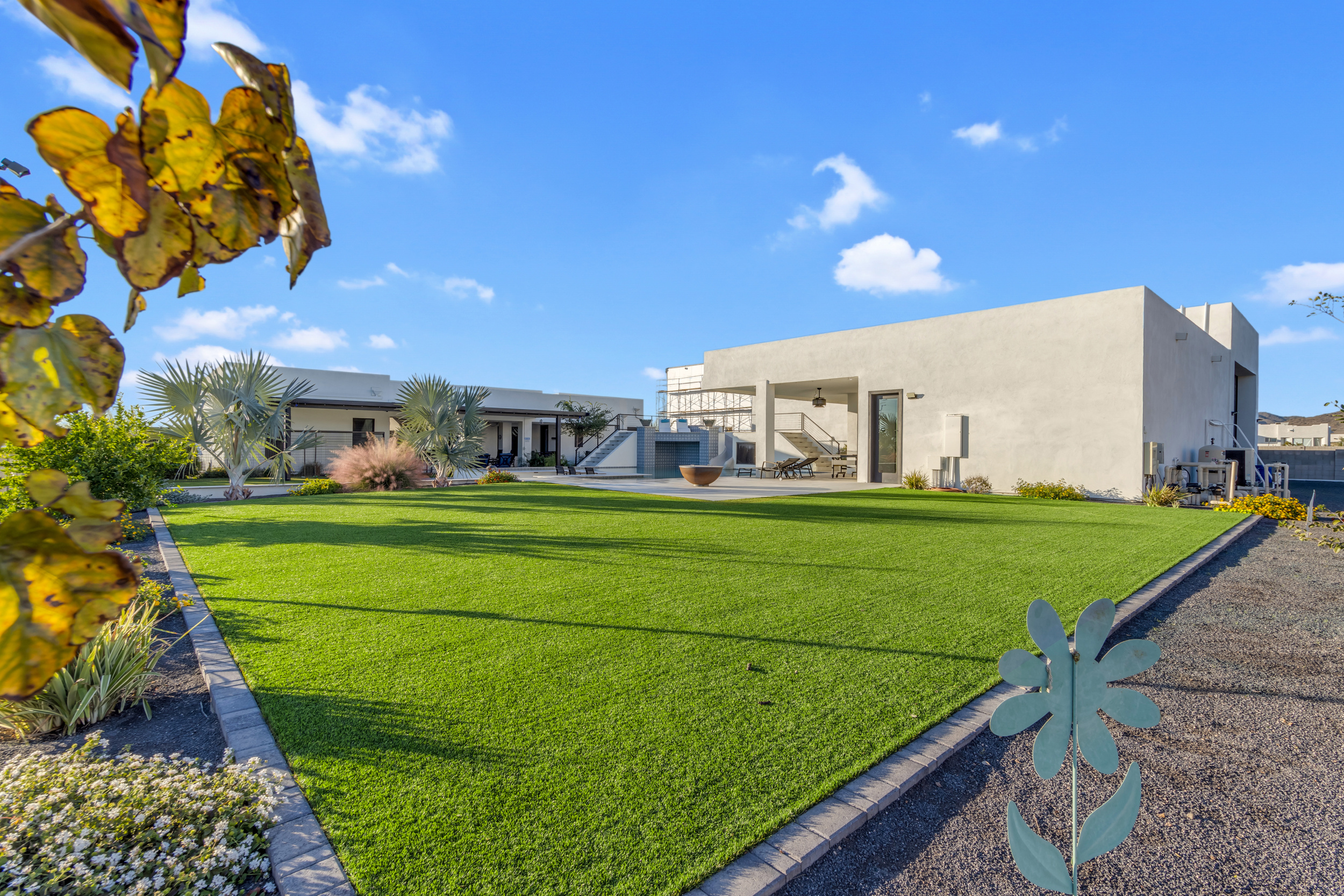 Modern white building with large green lawn, metal flower decoration, and clear blue sky.