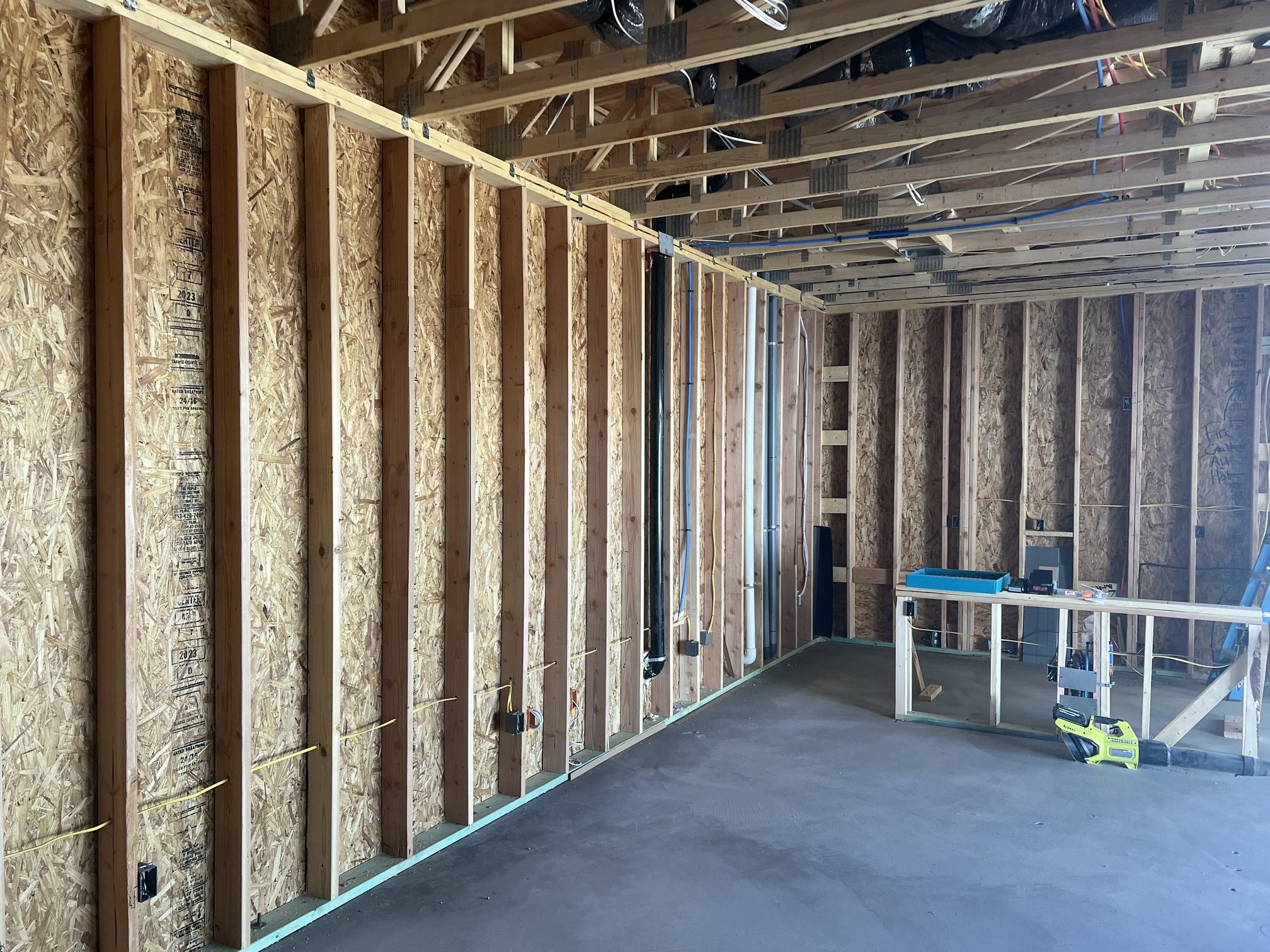 Interior view of a building under construction showing wooden framing, exposed wiring, and concrete floor.