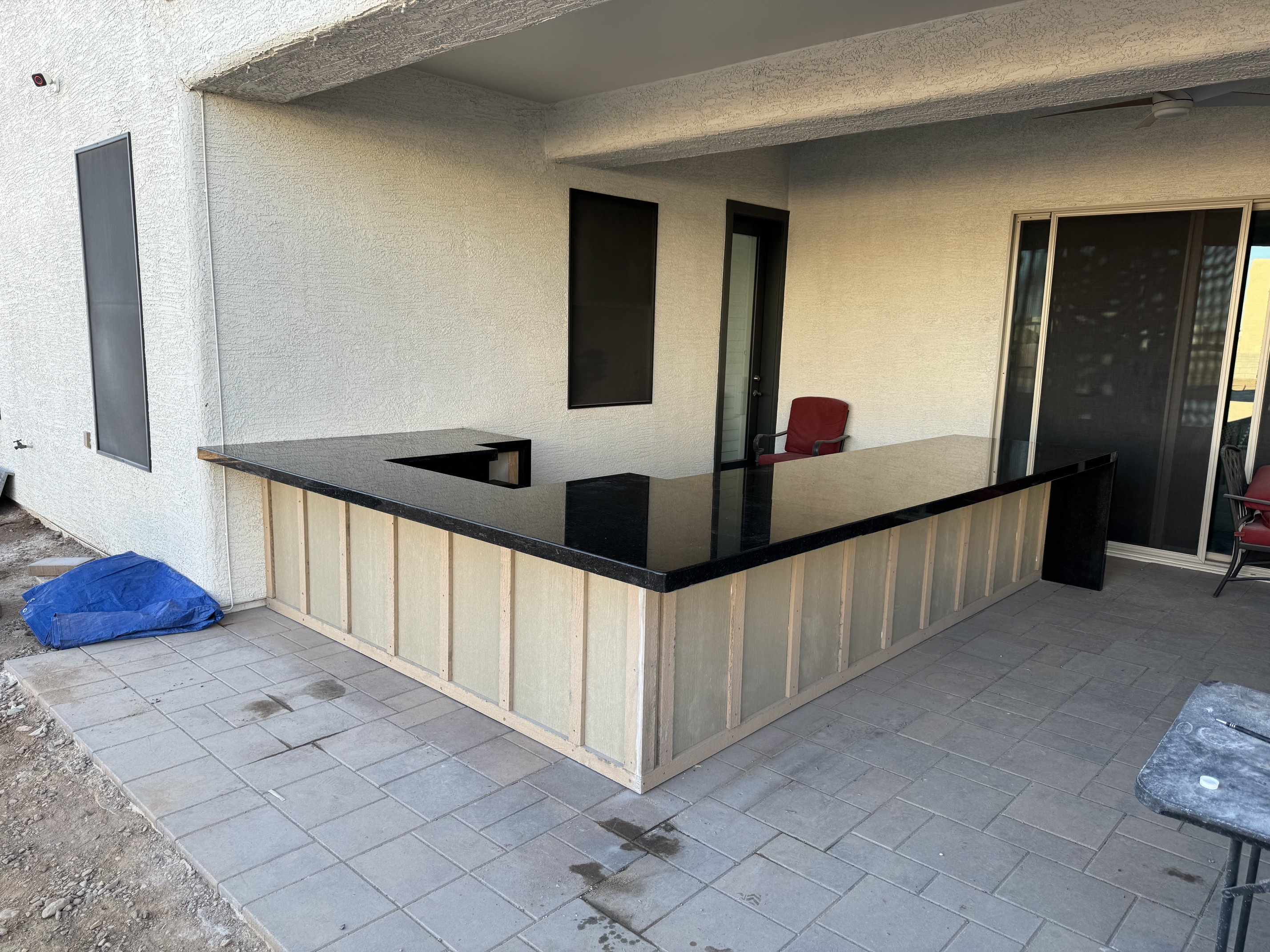 Outdoor patio bar with black countertop and wooden paneling under a covered area with tiled floor.