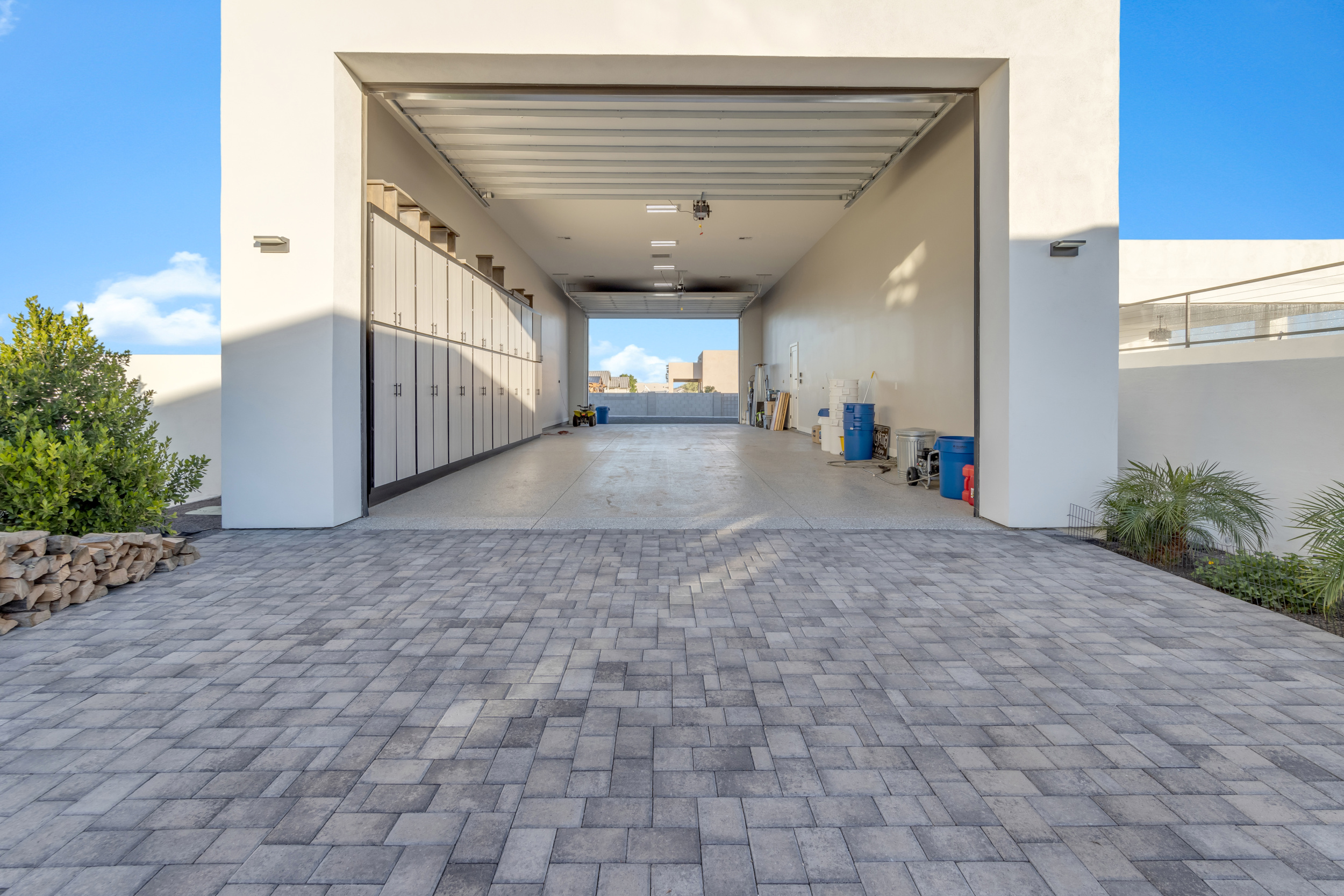 Spacious two-car garage with white cabinets on left and storage bins on right under open sky.