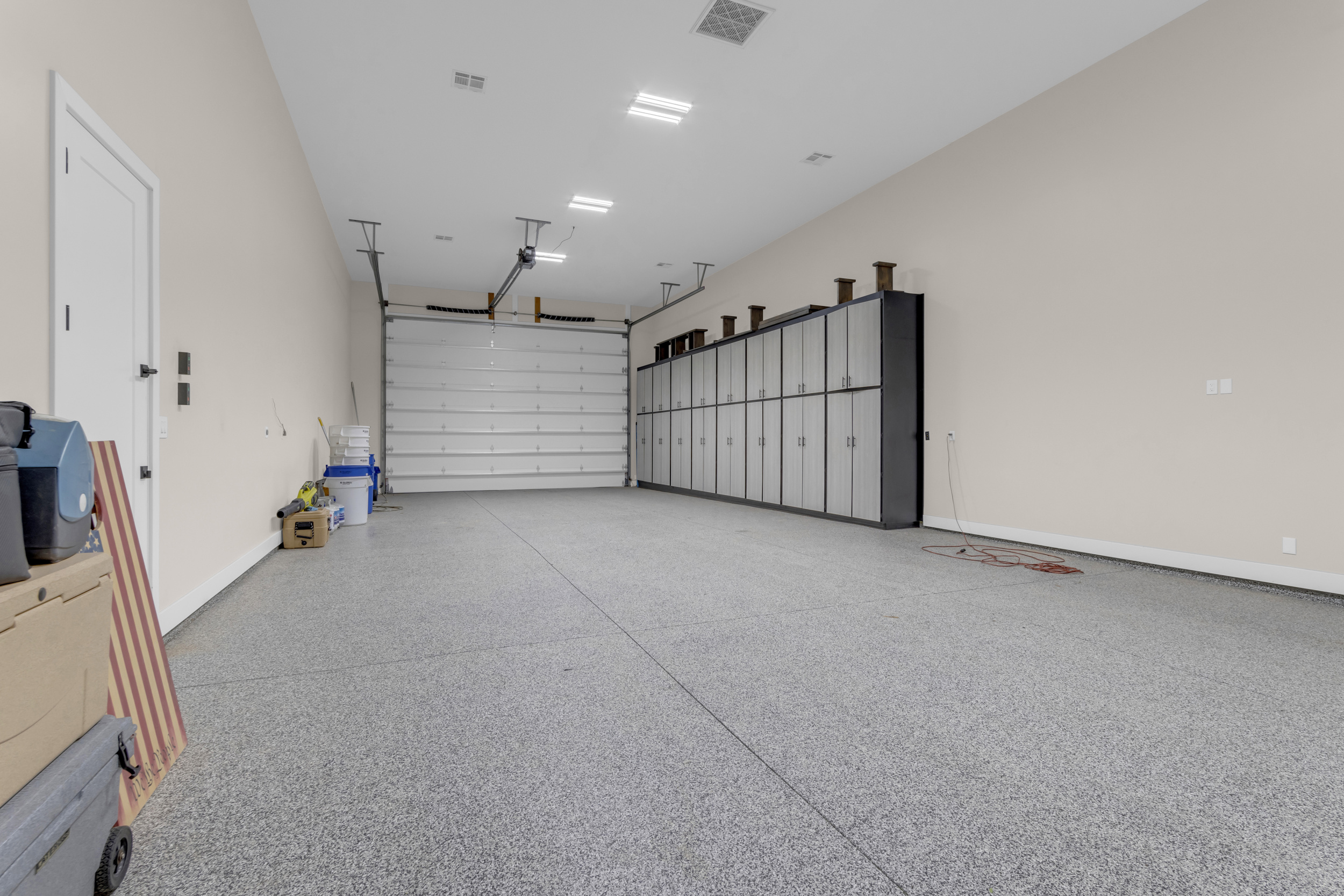 Empty large garage with closed white door, gray storage cabinets, and scattered items on walls and floor.