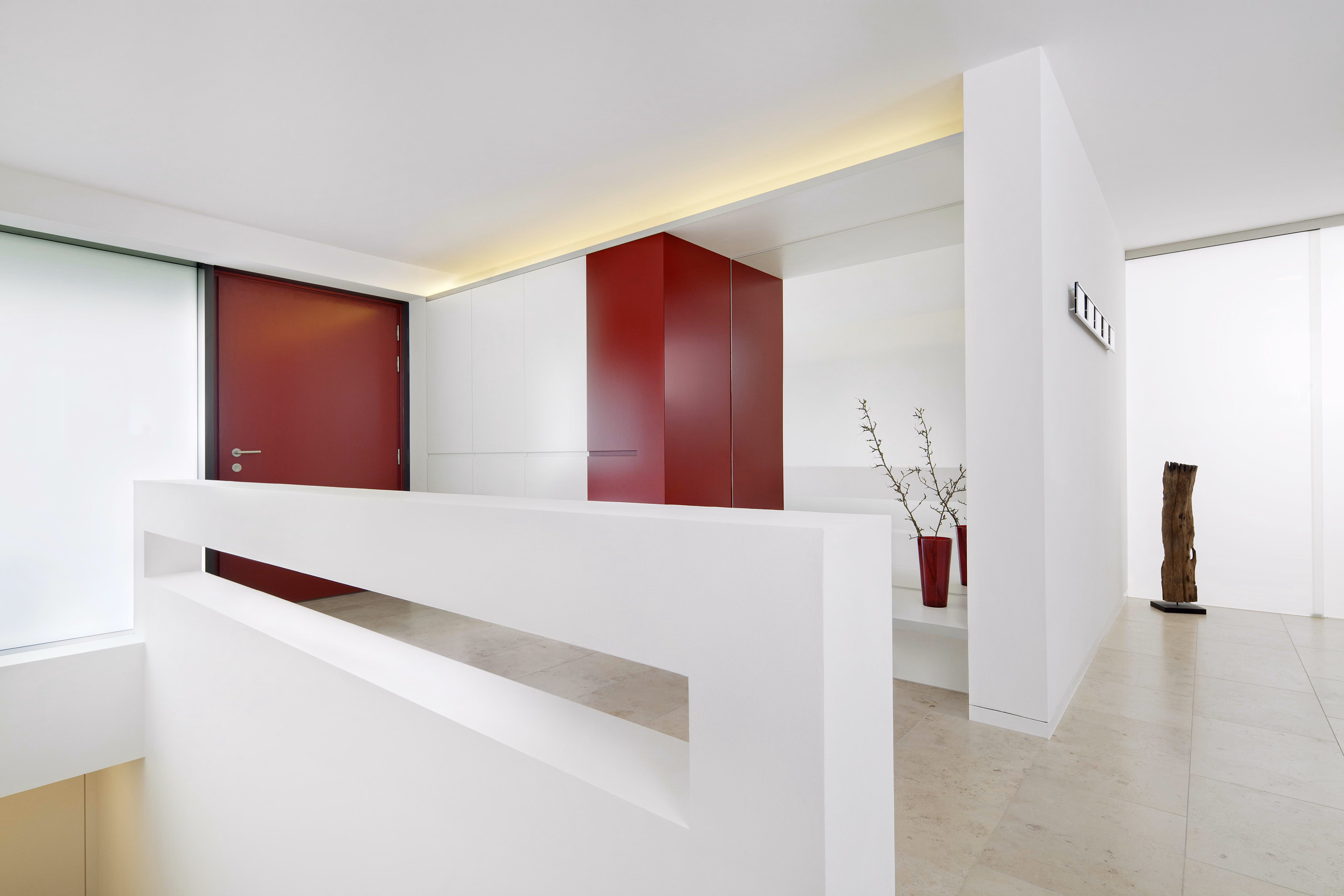 Minimalist white interior with burgundy door and cabinet and a red vase with branches.