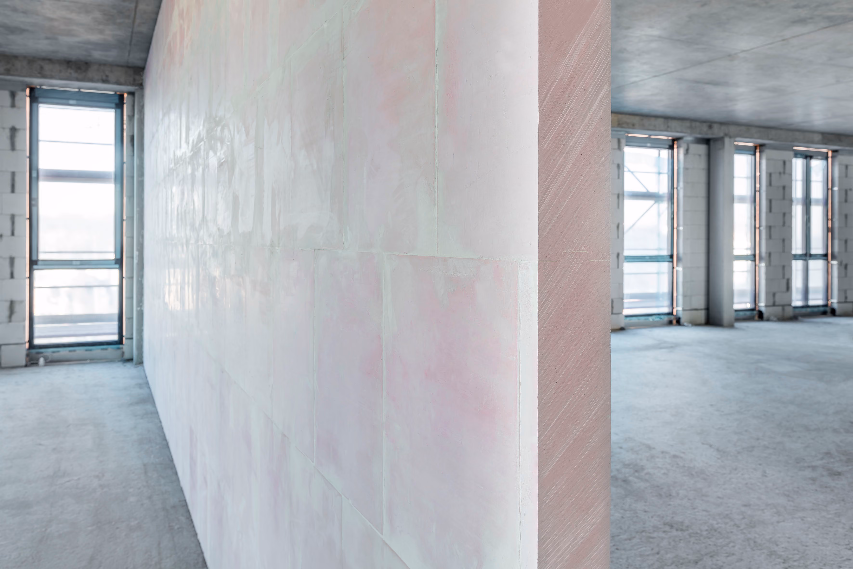 Interior of an unfinished modern building with concrete walls, floors, and large windows.