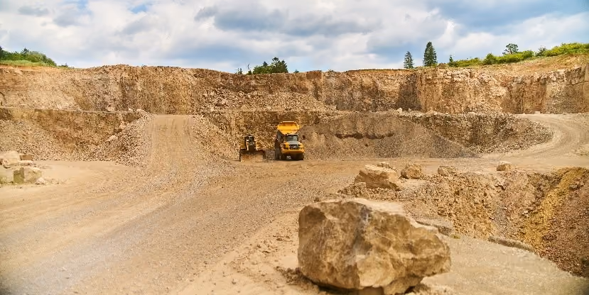 Quarry site with a large rock in foreground and heavy machinery near exposed rock walls.