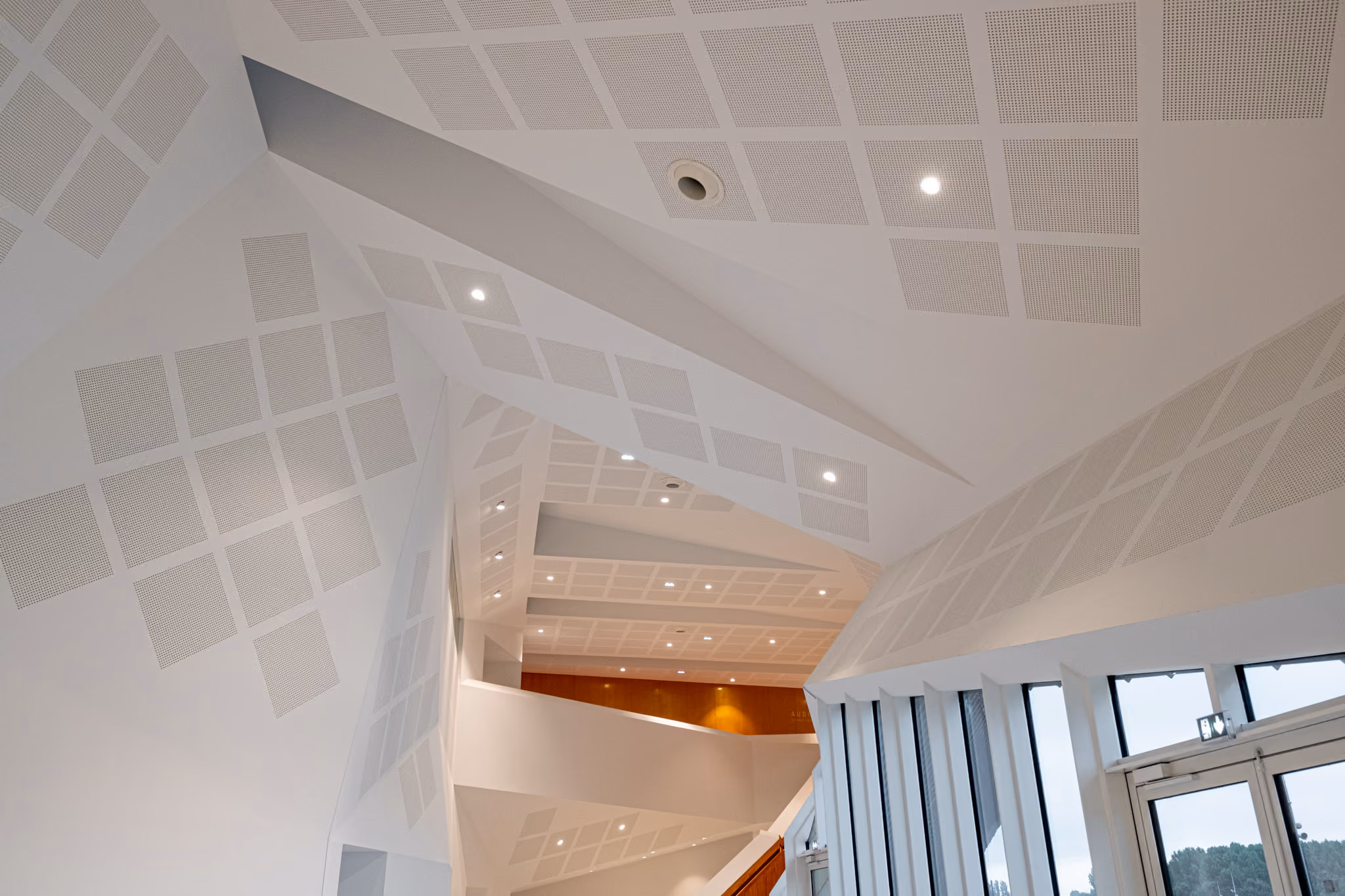 Modern interior with angular white ceiling panels, recessed lighting, and large windows on the right.