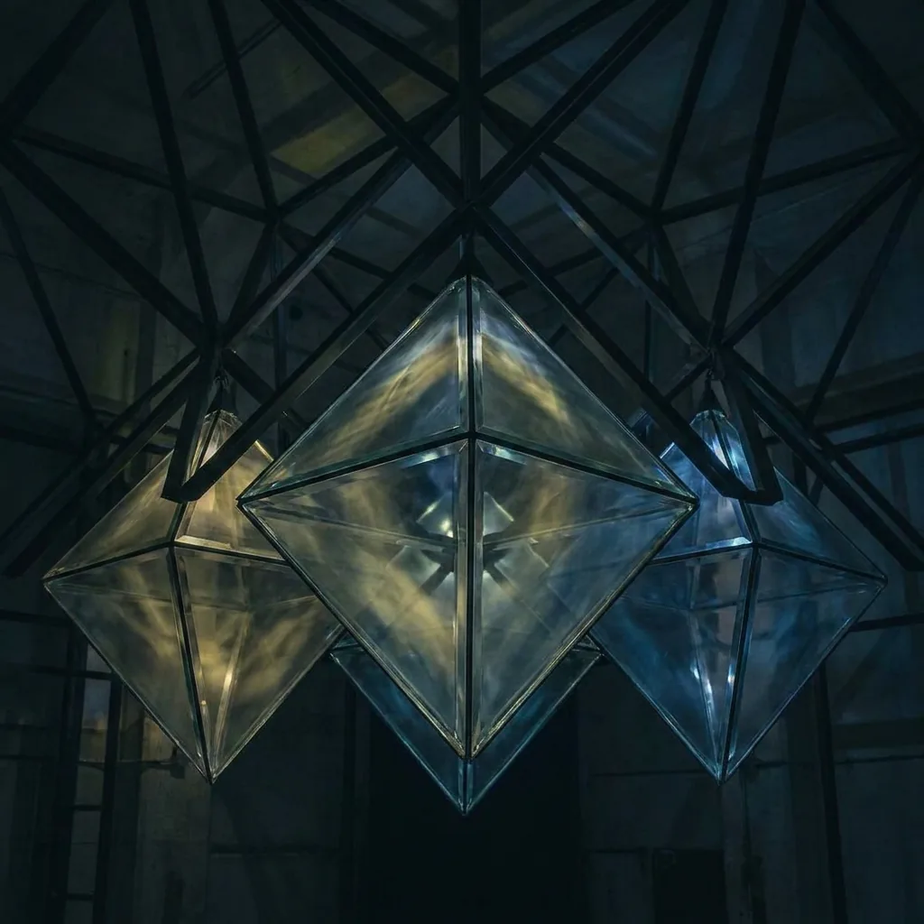 Faceted glass prototype forms suspended in a steel test frame, lit from within