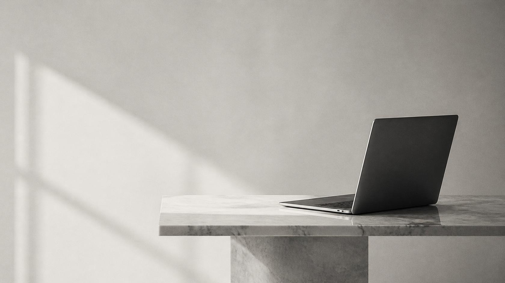 Open laptop placed on the right side of a marble table against a plain, softly lit wall.