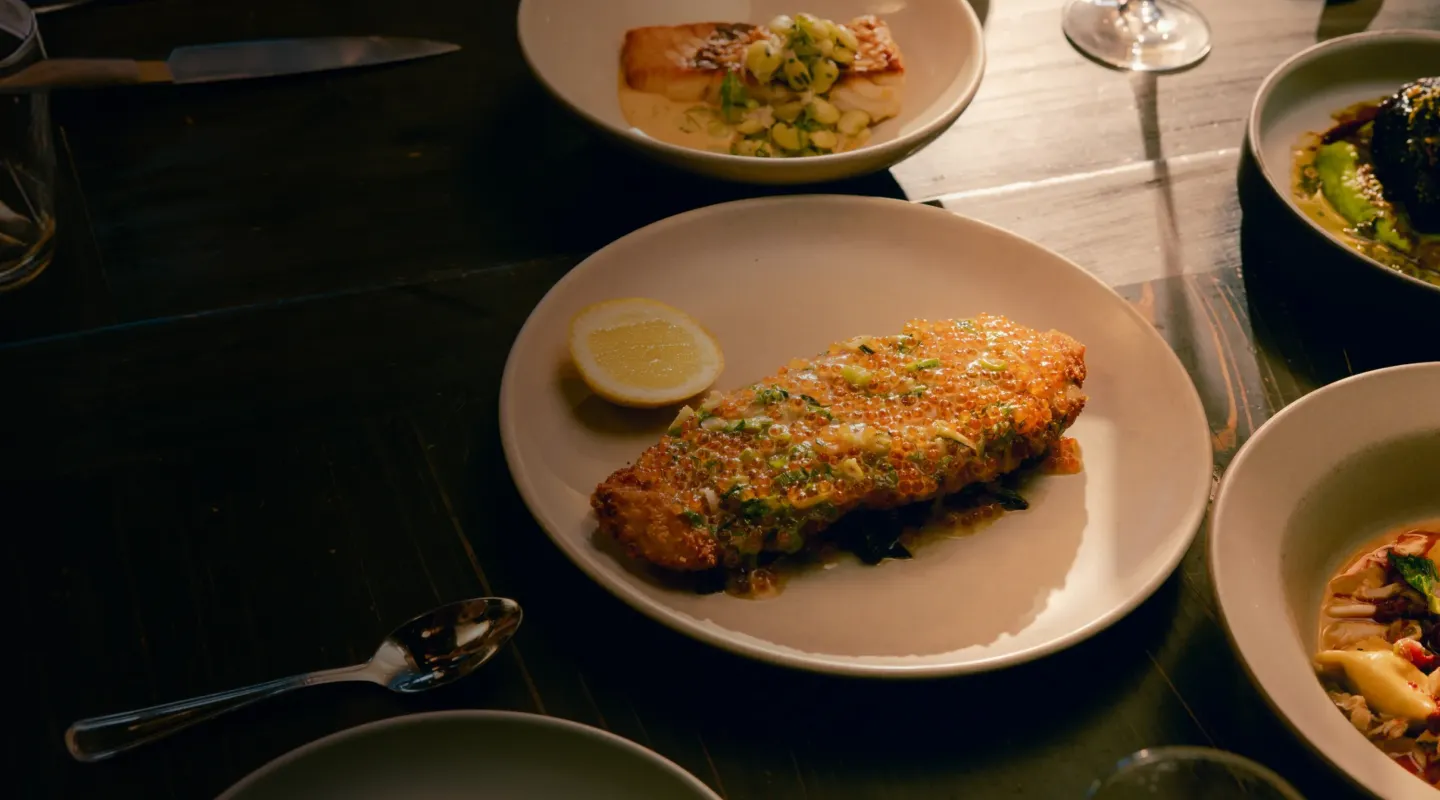 Plate with a golden crispy fish fillet topped with herbs and a lemon wedge on the side.