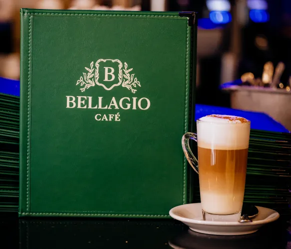 Green Bellagio Café menu next to a layered latte macchiato with foam on a saucer.