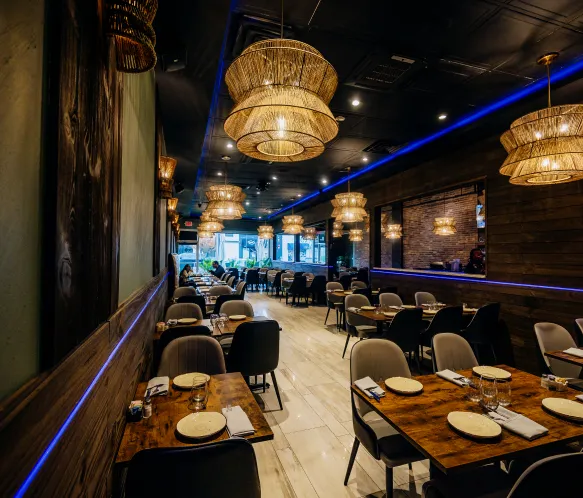 Cozy modern restaurant interior with wooden tables, chairs, and hanging wicker lamps.