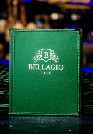 Green Bellagio Café menu with white logo on a reflective surface against a blurred background.