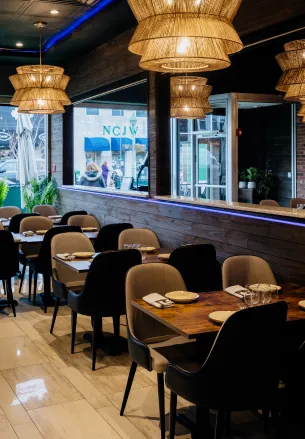 Cozy restaurant interior with dark chairs, wooden tables, and large woven pendant lights above.