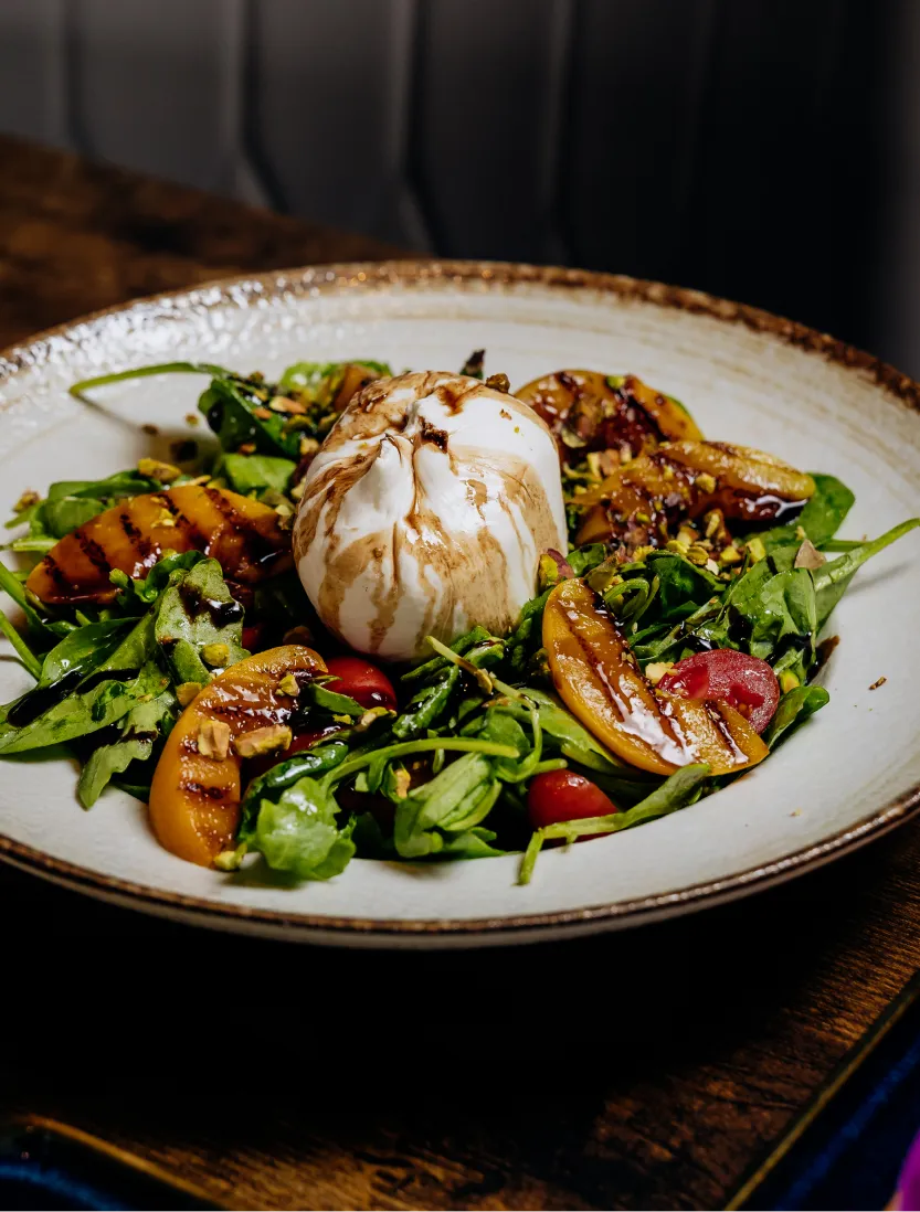 Salad with grilled peaches, cherry tomatoes, greens, nuts, and burrata cheese topped with balsamic glaze.