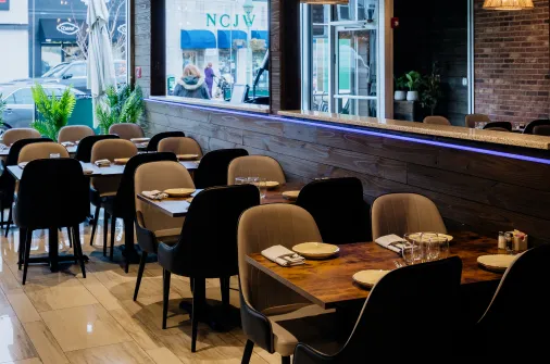 Inside of an empty restaurant with neatly set wooden tables and cushioned chairs under ambient lighting.