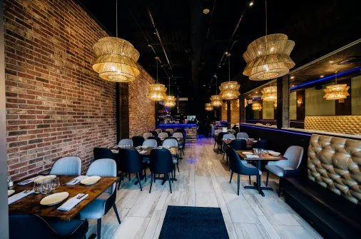 Modern restaurant interior with brick walls, hanging lamps, black and blue chairs, and marble floors.