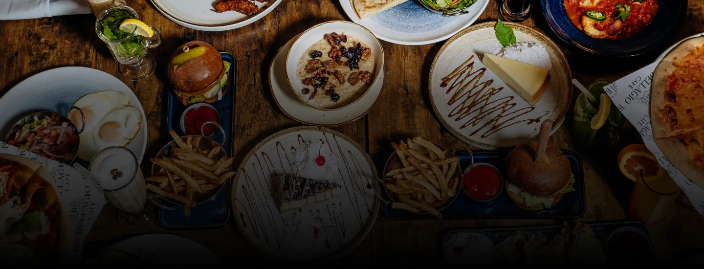 Table with burgers, fries, cheesecake, oatmeal, eggs, pizza, and drinks on wooden surface.