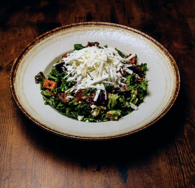 Salad with greens, diced vegetables, nuts, and shredded white cheese on a rustic plate.