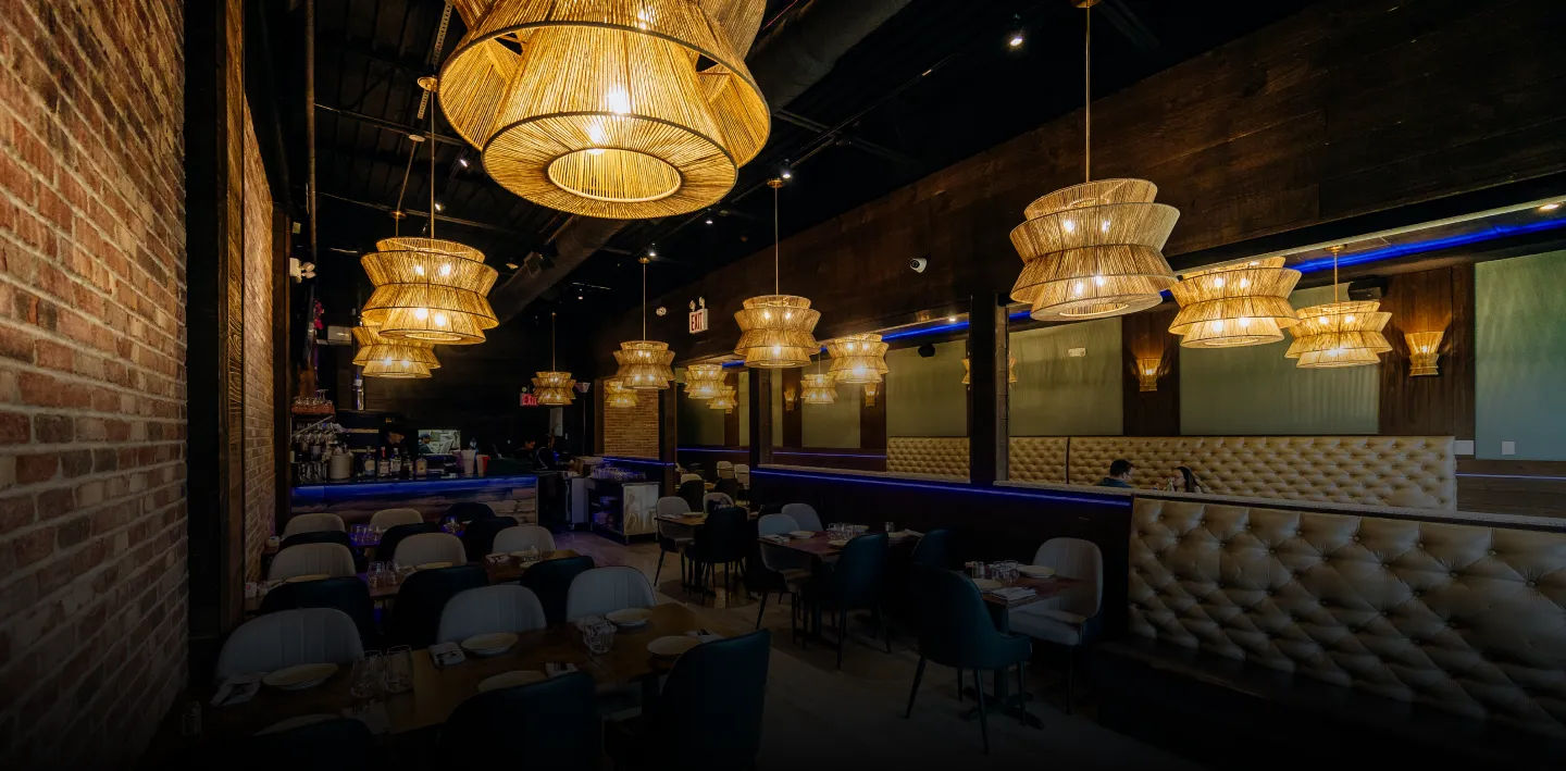 Cozy restaurant interior with hanging woven lamps, tufted booth seating, and exposed brick walls.