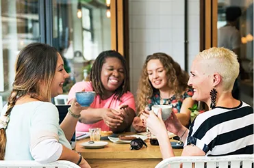 Four women smiling and talking while enjoying coffee at a café table.