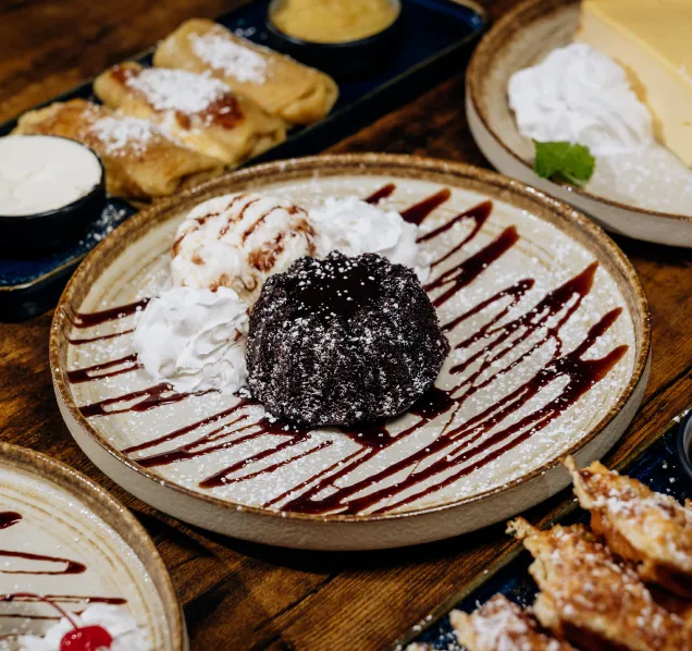 Chocolate lava cake with whipped cream, ice cream, and chocolate drizzle on a rustic plate.
