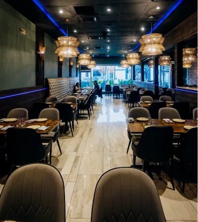 Empty modern restaurant dining area with tables, chairs, and hanging decorative lamps.