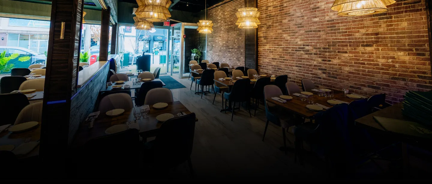 Interior of a modern restaurant with wooden tables, chairs, pendant lights, and brick wall.