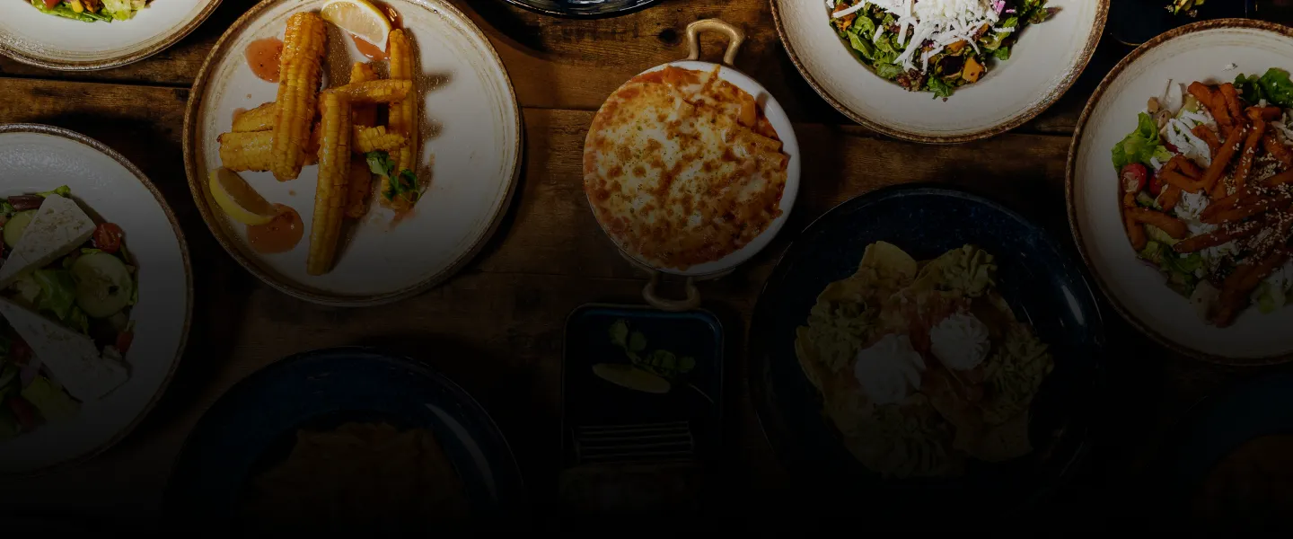 Multiple plates of diverse dishes including corn, salad, and a baked cheese dish on a wooden table.
