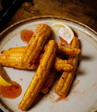 Grilled corn on the cob with sauce and a lemon wedge on a ceramic plate.