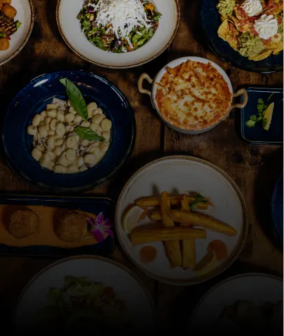 Top view of assorted dishes including pasta, salad, fries, and dips on a wooden table.
